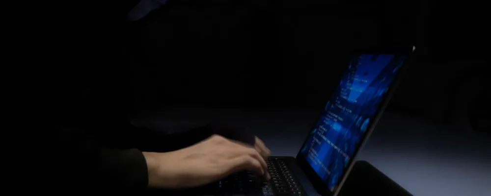 Pessoa digitando em notebook com tela azul em ambiente escuro.